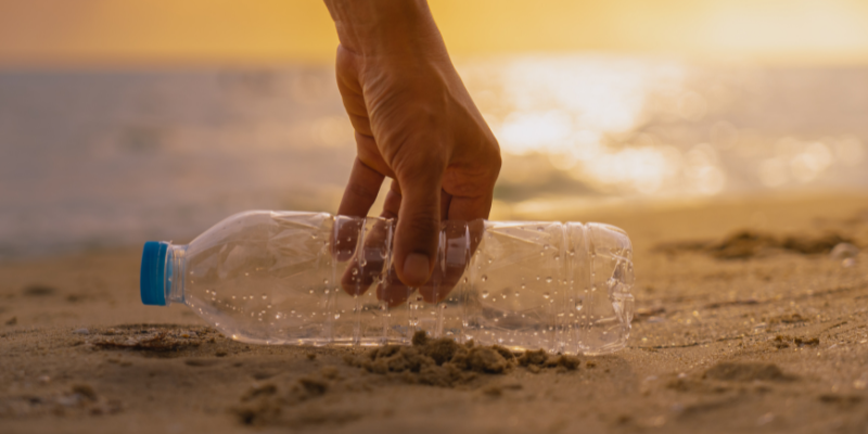 Beach Cleanup Picture of someone picking up plastic bottle at the beach.