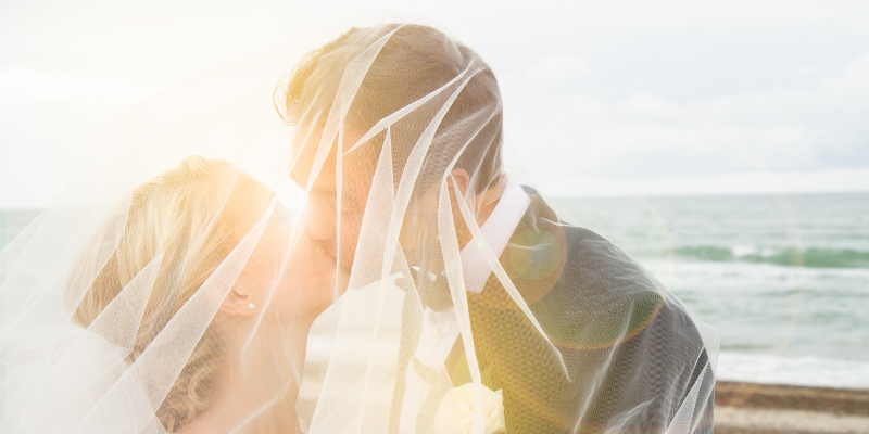 Outer Banks Beach Wedding Couple on the beach kissing in front of ocean under wedding veil.