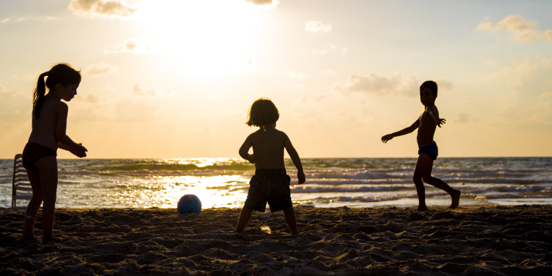 Silhouettes of 3 children playing on a dark beach at sunset.